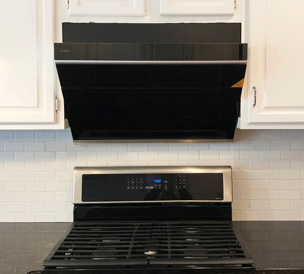 Onyx Black Tempered Glass JQG05 Series under cabinet range hood above a black stove in a white kitchen.