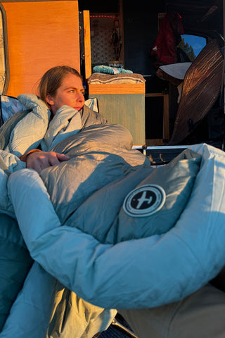 A woman lays by the side of her camper van, covered in an Aeronaut Hoverquilt