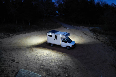 A camper van illuminating a clearing in a forest.