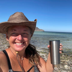 Author Erin Davy holds a cup with a view of the ocean behind her.