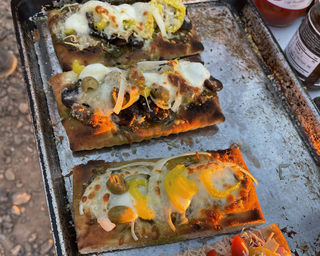 A tray of baked flatbread pizzas with an assortment of ingredients on a table outside.