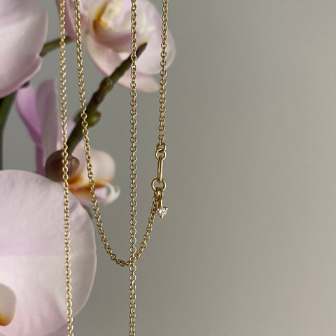 a dainty gold chain necklace with a diamond hung on an orchid branch, pink and white orchids in background