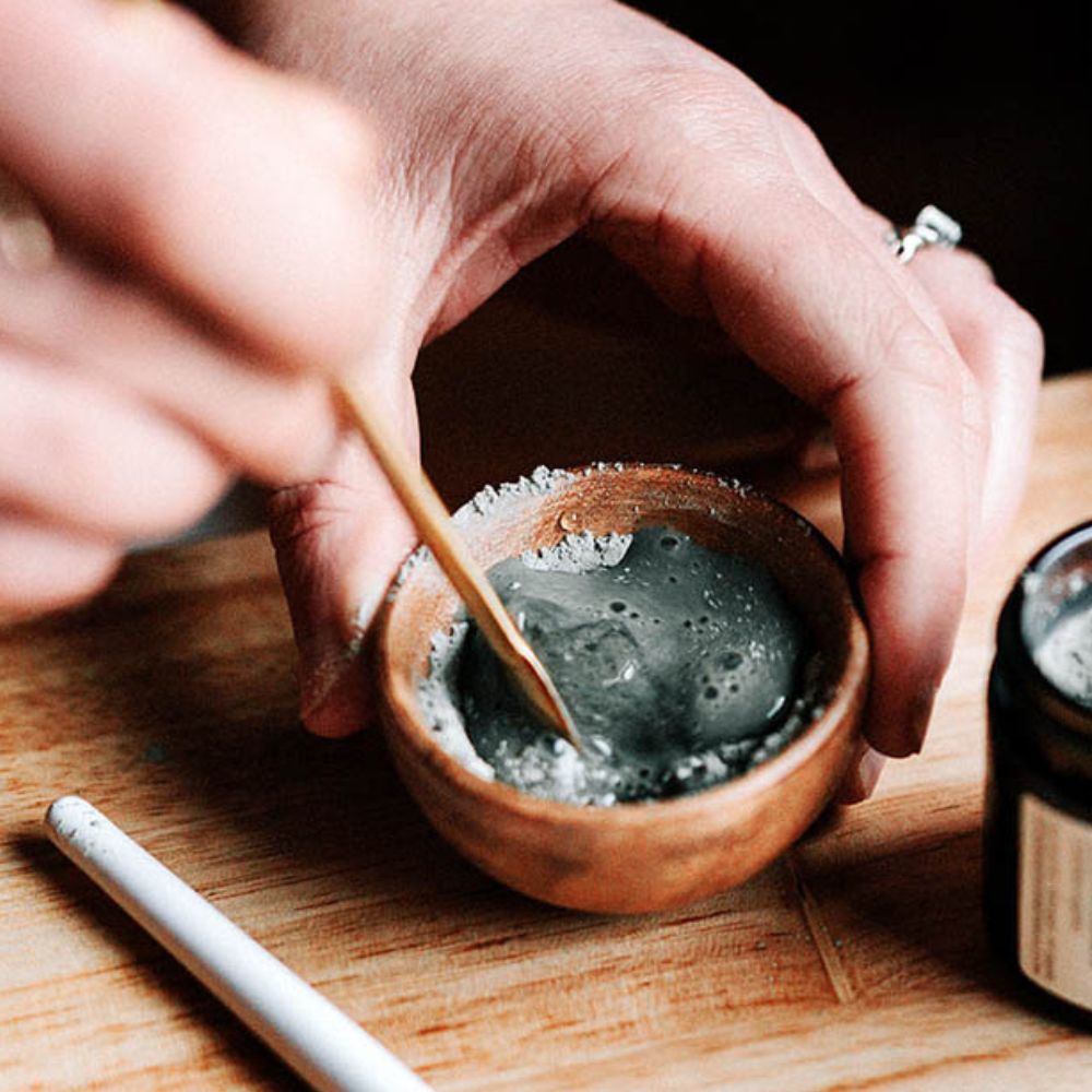 A woman mixes a small bowl of blue clay and kelp face mask