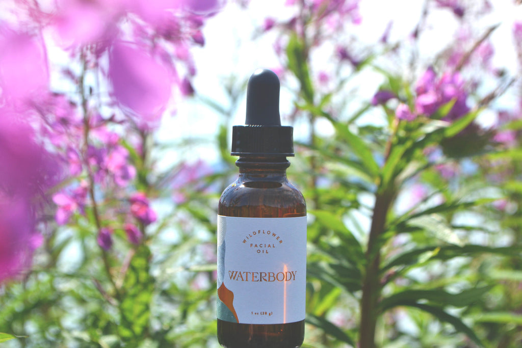a bottle Wildflower facial oil stands against a backdrop of magenta fireweed flowers