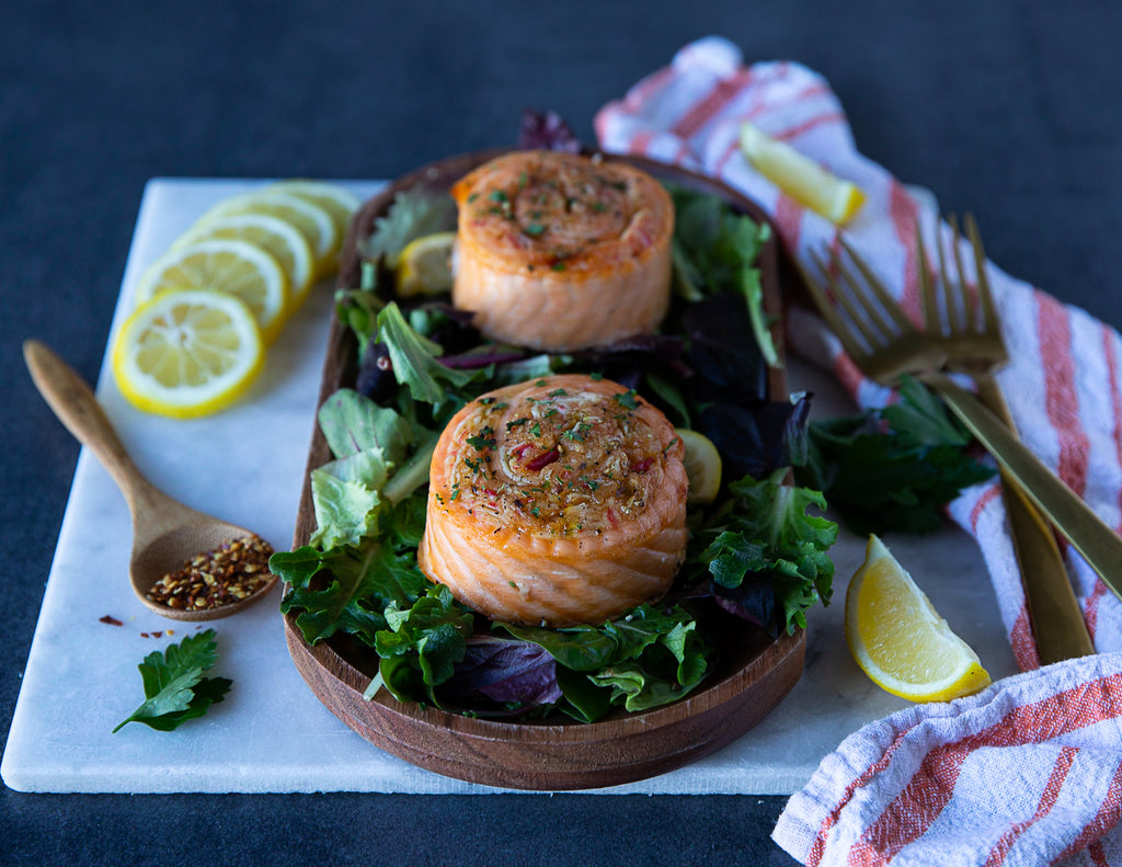 Salmon pinwheels plated on leafy greens.