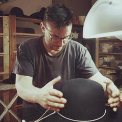 Inside the creative space of Agnoulita Hats, where tradition meets innovation. Surrounded by an array of tools, fabrics, and the gentle glow of a lamp, the setting is ripe for the birth of bespoke hats.