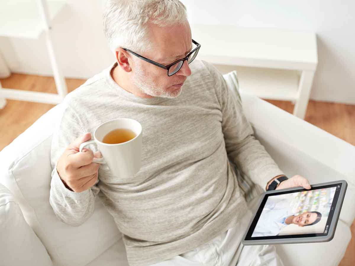 Elderly man talking to doctor on laptop while drinking tea