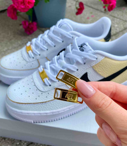 Gold shoe tags for air force 1 sneakers. Picture has a person holding two golden shoe charms for air force 1 sneakers.