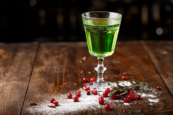 absinthe in cocktail glass on wooden table with sugar and red berries
