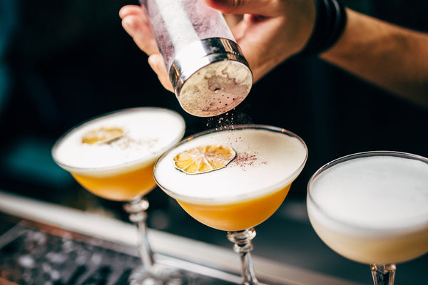 bartender garnishing three cocktails with cinnamon