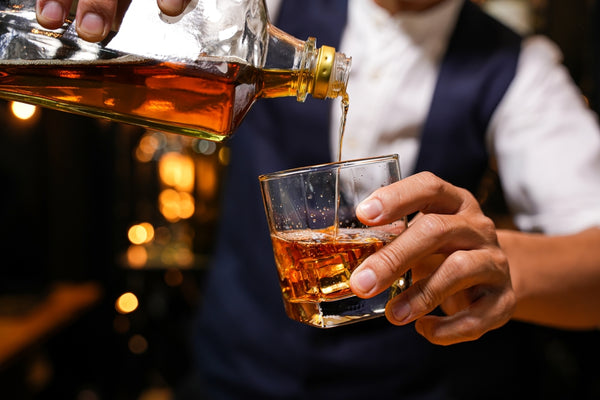 bartender pouring bourbon into cocktail glass from bottle