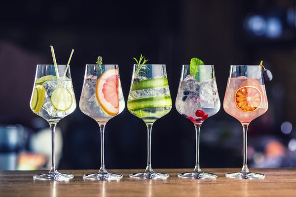 five different gin and tonic cocktails with fruit on bar