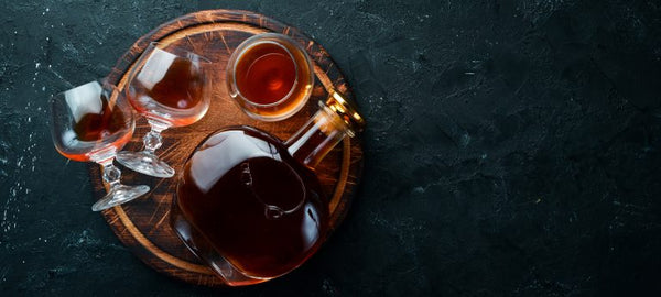 full bottle of cognac with three filled glasses on barrel