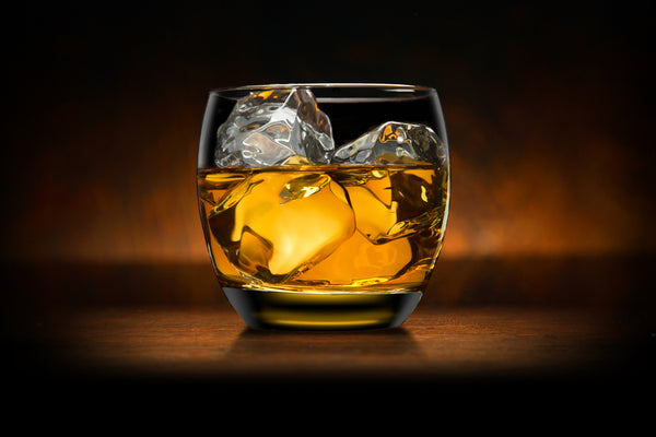 glass of bourbon with ice on wooden table with amber light