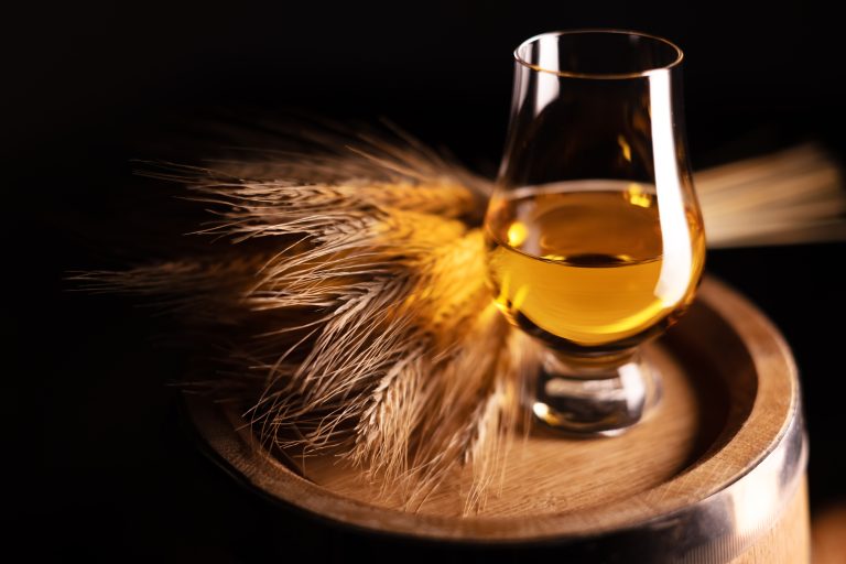 glass of rye whiskey on barrel beside rye