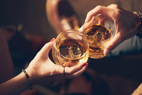 male and female hands toasting two glasses of bourbon