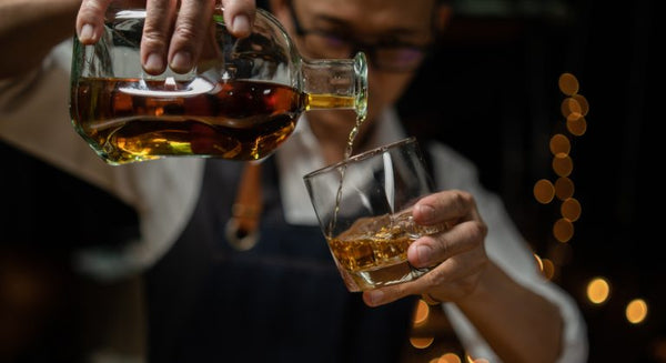 male bartender pouring bourbon from a glass bottle into a serving glass