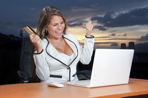 woman sitting in front of laptop with credit card in hand, smiling.