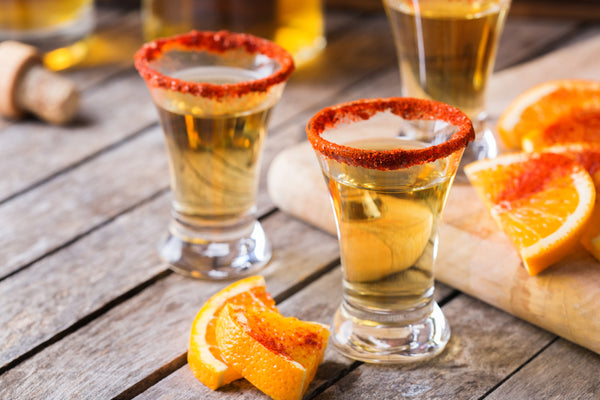 mezcal shots with chili powder and orange slices on wooden table