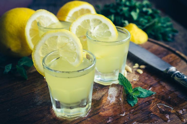 multiple shot glasses of limoncello with sliced lemons on cutting board with knife