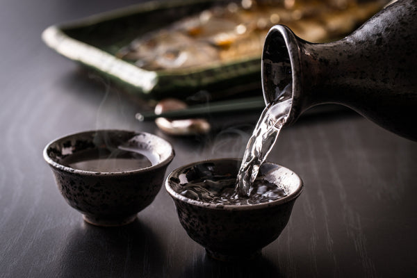 steaming sake being poured into two black sake cups on table