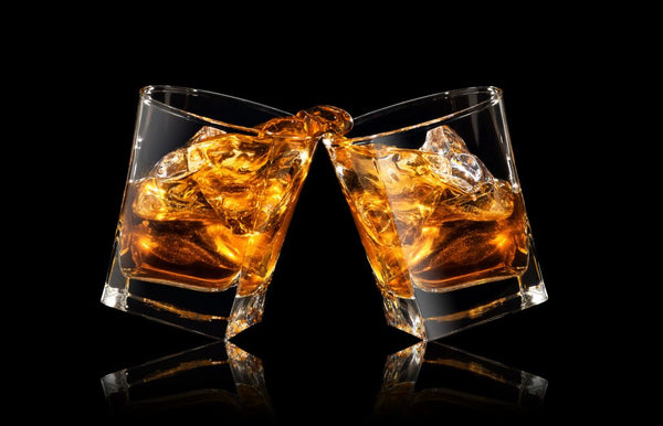 two cocktail glasses of whiskey clinking together with black background