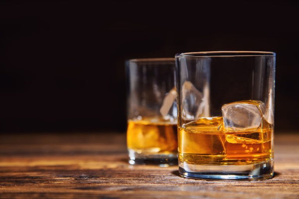 two glasses of bourbon with ice on wooden bar with black background