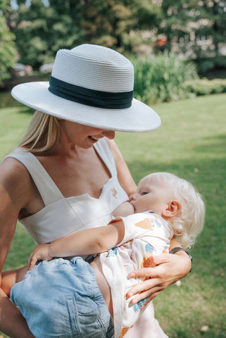 blond lady breastfeeding her son in a white top and a white hat