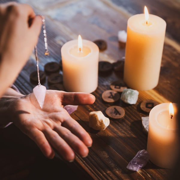 Tisch mit Kerzen und Hand, die ein Pendel hält