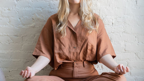 Blonde Frau mit brauner Kleidung sitzt zur Meditation