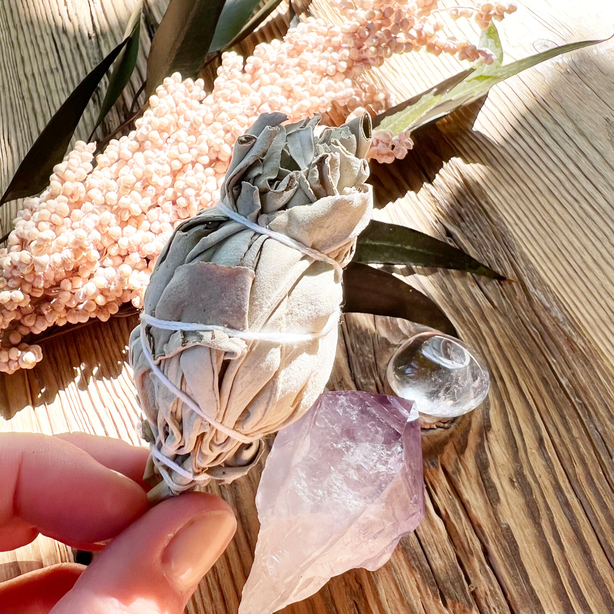 Hand hält Salbeifackel über Amethystspitze und Bergkristall-Trommelstein