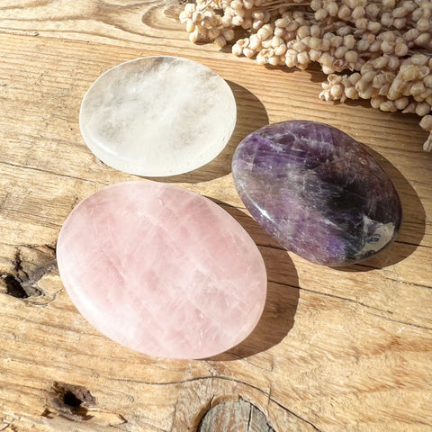 Drei Taschensteine aus Amethyst, Bergkristall und Rosenquarz auf einem Holztisch