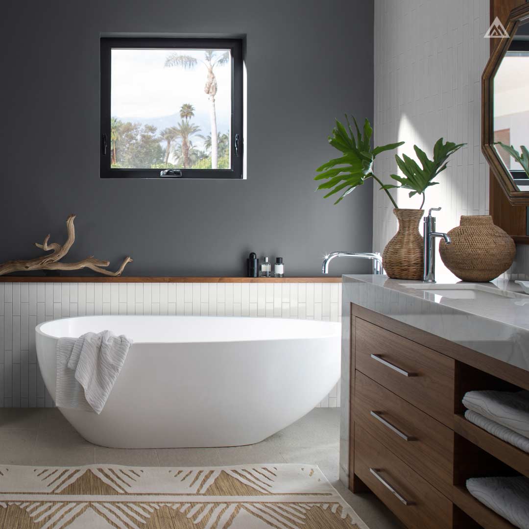 large, free-standing bathtub under square window overlooking palm trees with a house plant in a woven basket at the basin