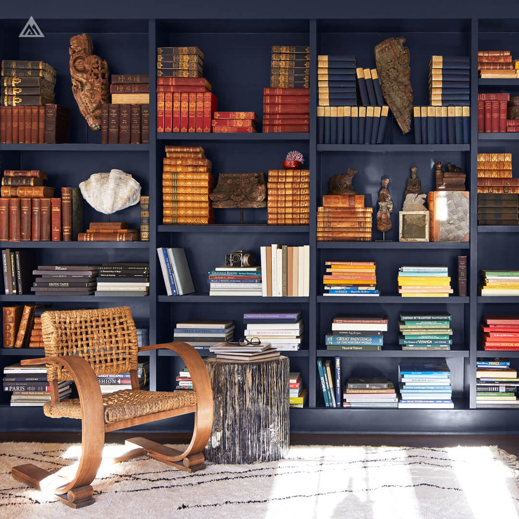 a sitting room with a chair, a wood stump table, and a full wall of navy blue coloured book shelves