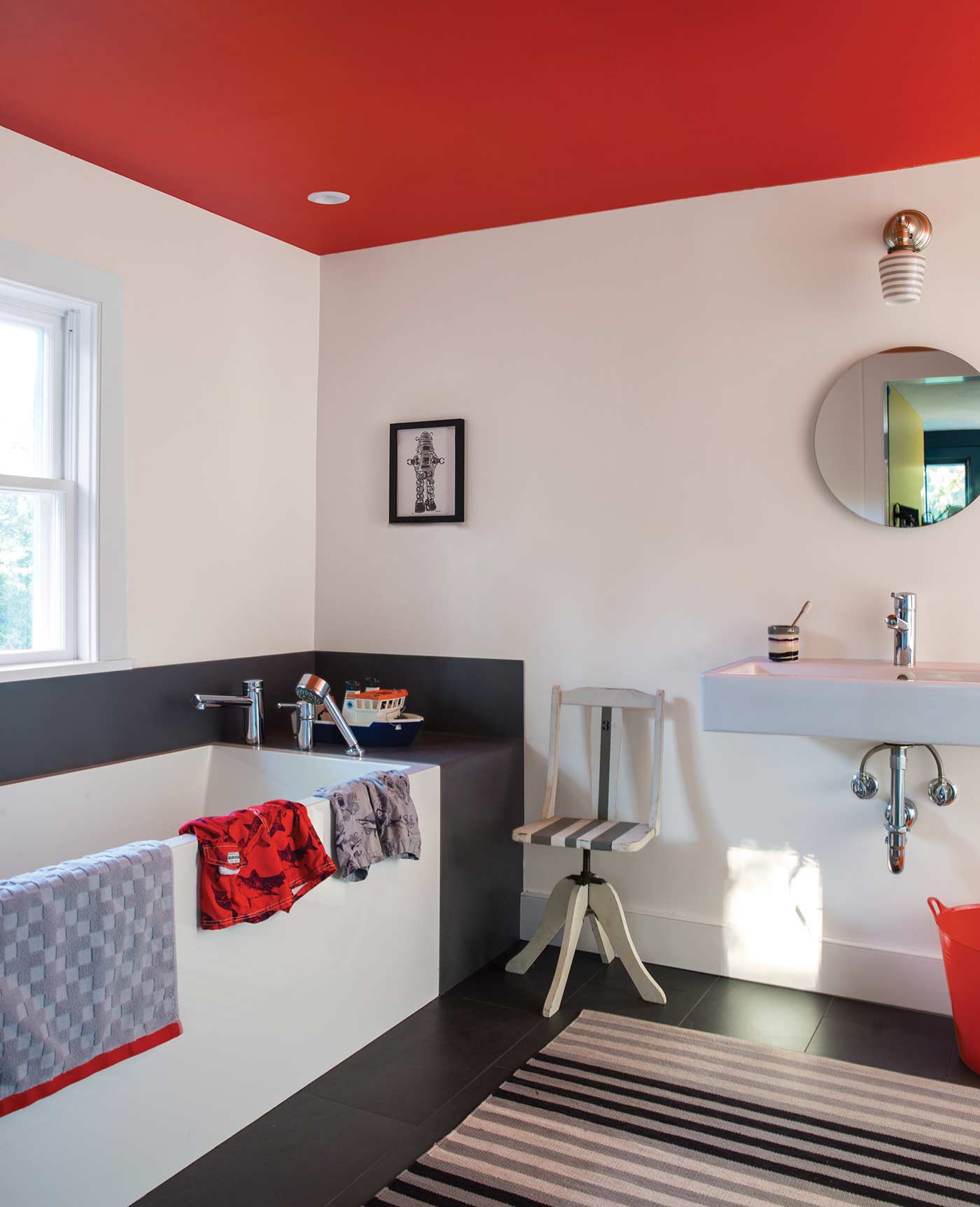white bathroom with a circular mirror above a basin, bath to the left and a red ceiling