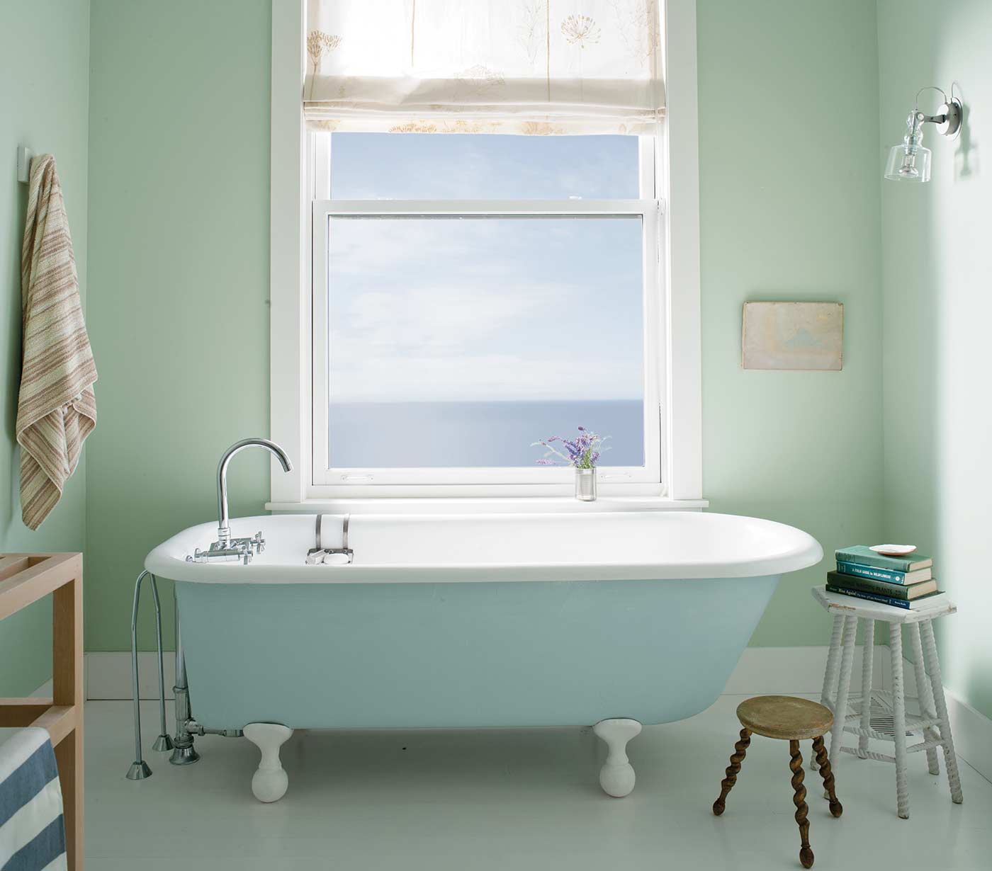 light blue and white bathtub on claw feet in front of a large frosted mirror