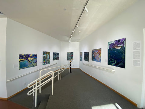 Photo of Julian Keller-King's Water Works exhibit in the Holter Museum of Art: eight large narrative illustrations hang along an angled ramp with a rail down the center.