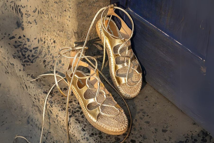 This is an image of a pair of Golden Gladiator Sandals for women placed on stairs