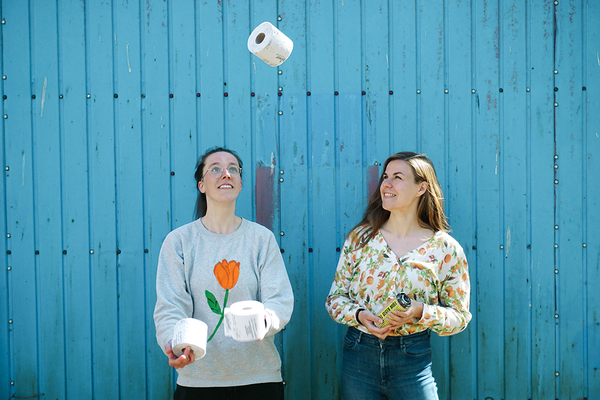 Maike und Katja starten im ASApreneur-Programm. Auf dem Foto stehen beide nebeneinander, Maike jongliert mit Klopapier-Rollen, Katja lacht.