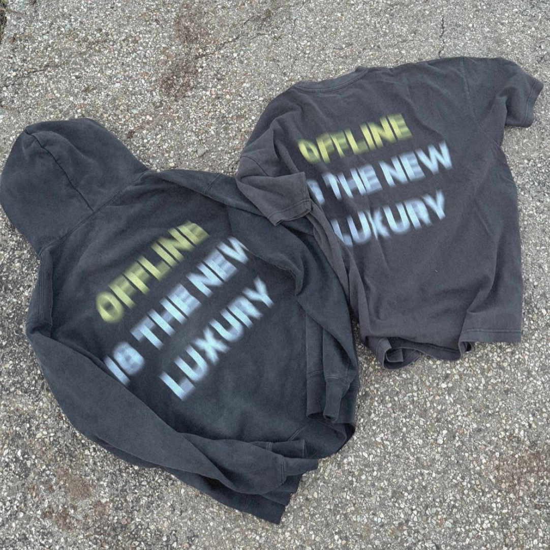 Two black hoodies with text 'OFFLINE IS THE NEW LUXURY' on concrete.