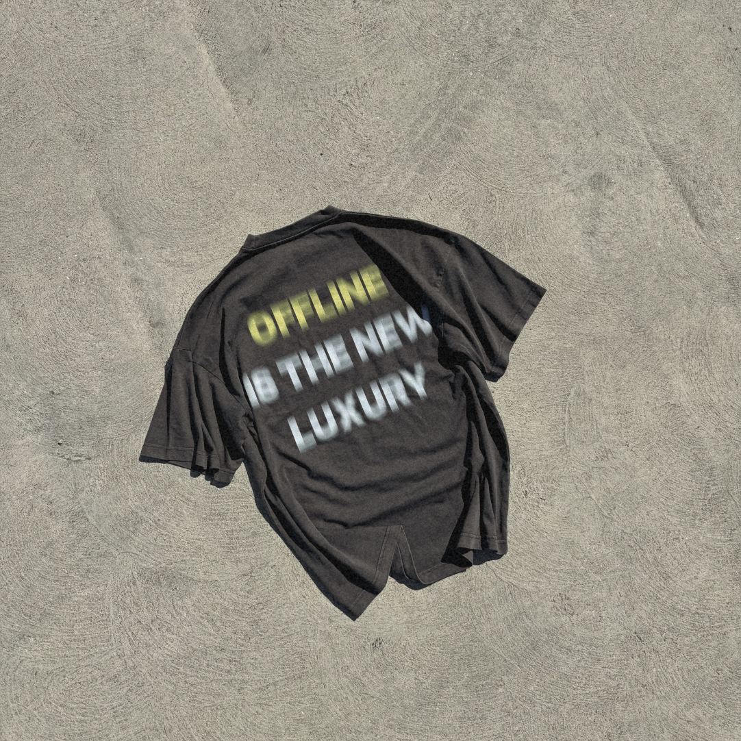 Black t-shirt with the phrase 'OFFLINE IS THE NEW LUXURY' laid out on a concrete surface.