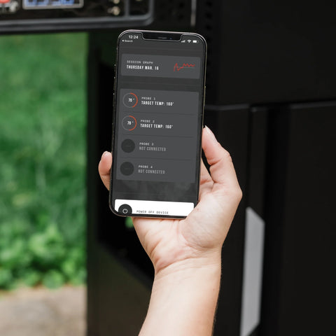 Someone holds a smartphone running the Masterbuilt App up in front of an AutoIgnite Grill and Smoker