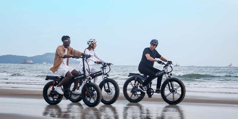 2 men  and 1 women ride engwe x20, x24 and x26 e-bikes on the beach