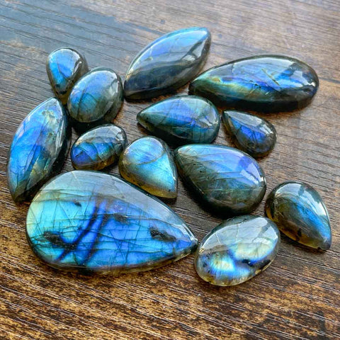 A group of blue/green labradorite gemstones in different shapes like ovals, tear drops, and marquis cut labradorites. 