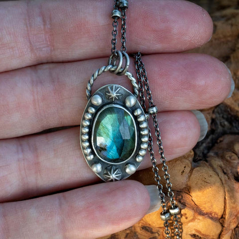 A pendant necklace with a green and blue flash rose cut labradorite framed by silver stars. The labradorite star necklace hangs from a beaded 18" chain in sterling silver. 