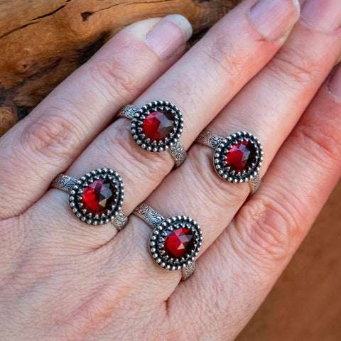 A hand wearing four red garnet birthstone rings