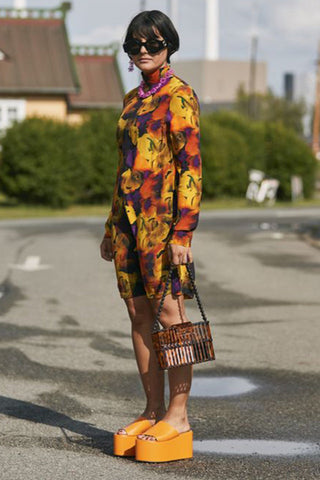 Girl wearing orange flatform slide sandals with printed dress.