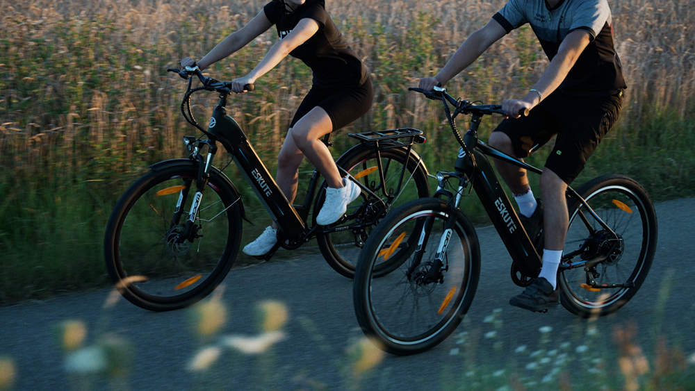 Ein Mann und eine Frau radeln mit ihren E-Bikes auf dem von Feldern umgebenen Weg