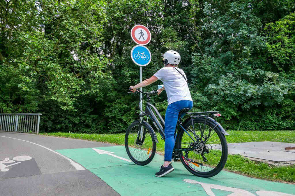 Eine Frau mit Helm fährt mit E-Bike auf dem Radweg