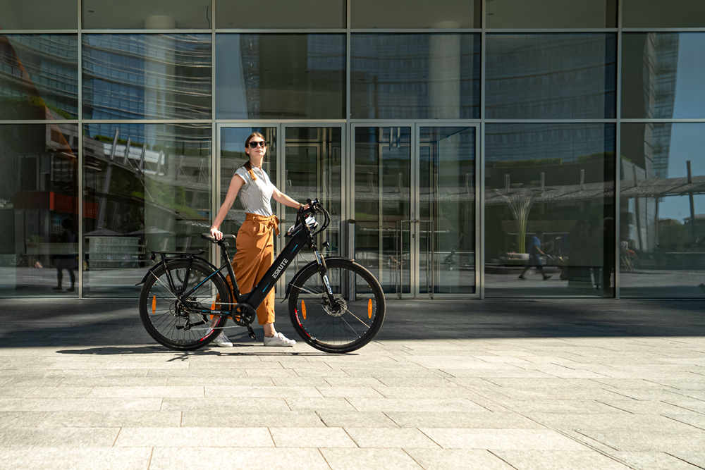 Eine Dame steht mit ihrem Elektrofahrrad vor einem Gebäude